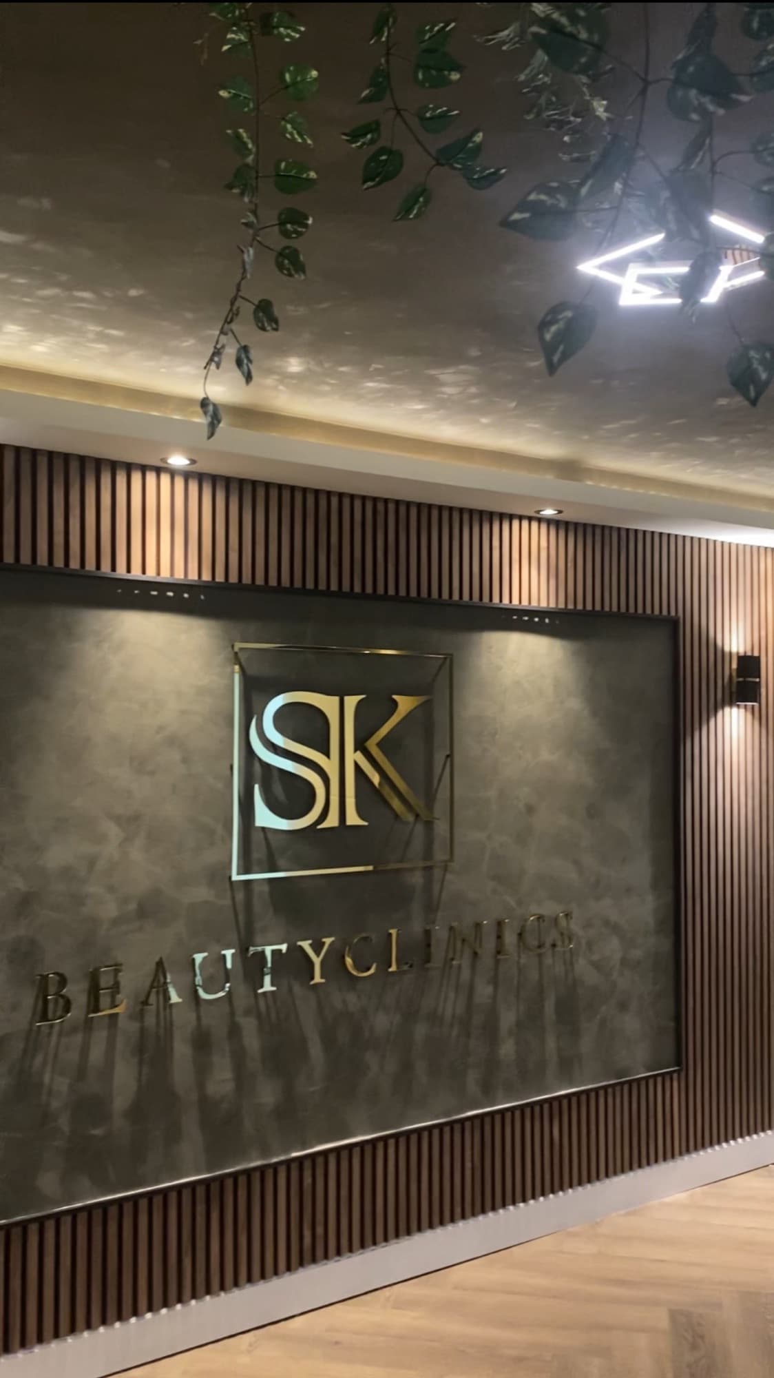 Interieur van SK Beautyclinics met het gouden SK-logo op een houten lambriseringswand